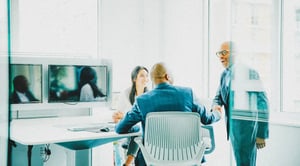 Two men shaking hands; one is sitting in an office chair, the other is standing